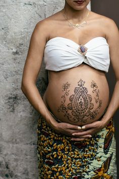 a pregnant woman wearing a white top and patterned skirt, with her belly covered in tattoos