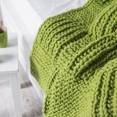 a green knitted blanket sitting on top of a bed next to a white table