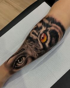 a person with a tiger eye tattoo on their arm and leg, sitting on top of a table