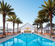 an outdoor swimming pool with lounge chairs and palm trees in the foreground, surrounded by white buildings