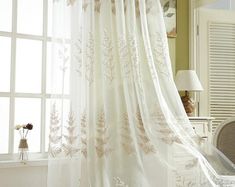 a white curtain hanging from the side of a window in front of a desk and chair