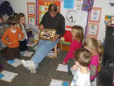 a group of children and an older man holding a cake in a room with posters on the walls