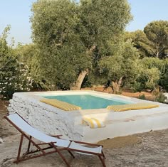 an empty lounge chair sitting next to a pool in the middle of a field with trees