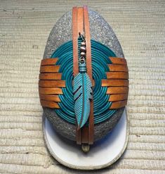 a stone with a feather on it sitting on top of a white plate next to a brown leather belt