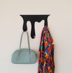 a purse and coat hang on the wall next to a hook that is shaped like a dripping paint