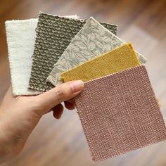 a person holding four different colored samples of fabric in their hands on a wooden floor