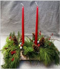 two red candles sitting on top of a wooden box filled with greenery and pine cones