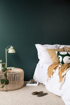 a bedroom with green walls, white bedding and a wicker basket on the floor