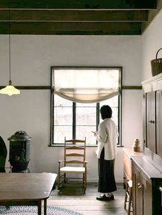 a woman standing in a kitchen next to a table and chair with an open window