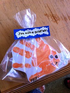 a plastic bag with an orange cat in it on top of a wooden table next to someone's feet