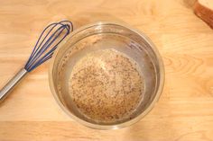 a metal bowl filled with brown liquid next to a whisk on top of a wooden table