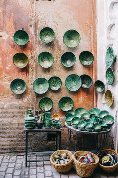 green plates and bowls are on display in front of a wall that is covered with clay tiles