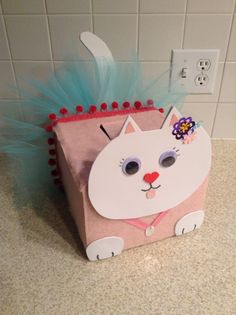 a paper bag shaped like a cat with blue feathers on its head and ears, sitting on a counter