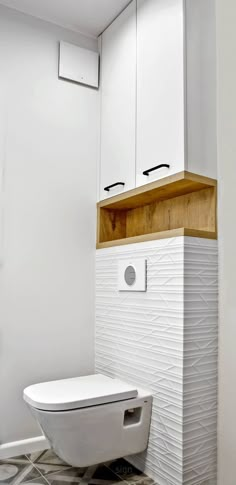 a white toilet sitting inside of a bathroom next to a wooden cabinet and tiled floor