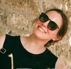 a woman wearing sunglasses is smiling and holding a drink in front of a brick wall