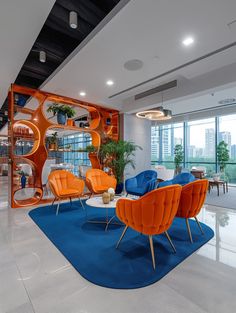 an office with orange chairs and blue rugs in front of glass walls that look out onto the city