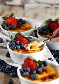 three bowls filled with pudding and berries on top of a blue place mat next to a person's hand