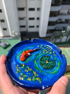 a hand holding a blue plate with a fish on it and some buildings in the background