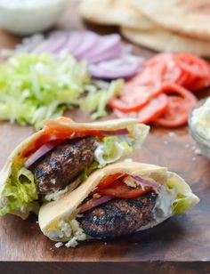 two hamburgers with lettuce, tomatoes and onions on a wooden cutting board