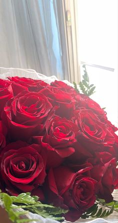 a bouquet of red roses sitting on top of a white cloth covered table next to a window