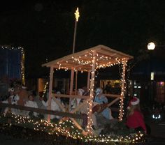 people dressed as santa clause riding on a float in the street at night with christmas lights all around