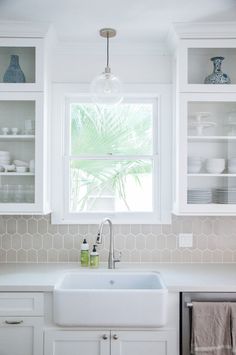 a kitchen sink sitting under a window next to white cabinets