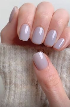 a woman's hand with light gray nail polish on her nails and a white sweater