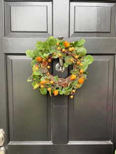 an orange wreath hangs on the front door of a gray house with green leaves and red berries