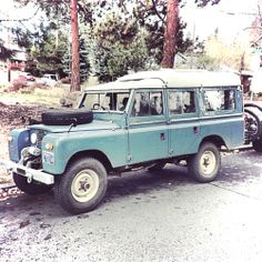 an old blue land rover is parked on the side of the road in front of some trees