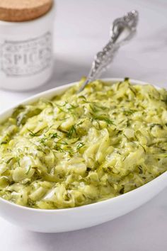 a white bowl filled with green food next to a spoon