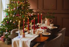 a dining room table set for christmas dinner with candles on the table and presents under the tree