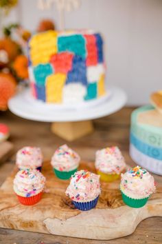 cupcakes with sprinkles are sitting on a cutting board next to a cake