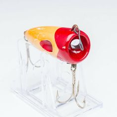 a red and yellow fishing lure sitting on top of a plastic stand with hooks attached to it