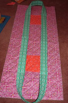 a pink and green yoga mat laying on the floor next to a book bag with an orange ribbon