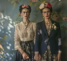 two women in formal clothing standing next to each other with flowers on their head and hands