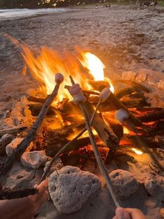 someone roasting marshmallows over an open fire on the beach