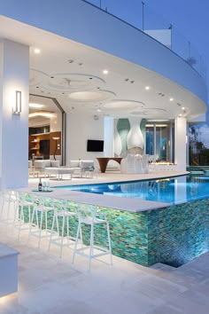 an indoor swimming pool in the middle of a large living room with white chairs around it