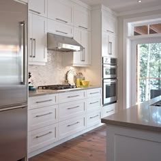 a large kitchen with white cabinets and stainless steel appliances, along with wood flooring