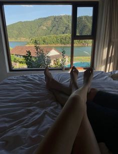 a woman laying on top of a bed in front of a window next to a lake