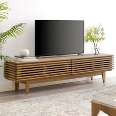 a flat screen tv sitting on top of a wooden entertainment center next to a potted plant