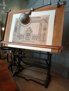 an old fashioned drawing on display in a room with wooden tables and stools next to it