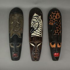 three african masks sitting next to each other on a white surface with black and brown designs