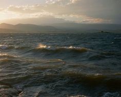 the sun is setting over the ocean with mountains in the background