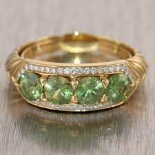 a gold ring with green and white stones on it's sides, sitting on top of a table