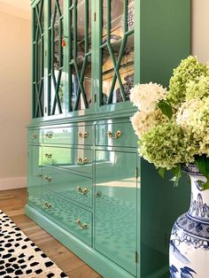 a blue and white vase with flowers on top of it next to a green china cabinet