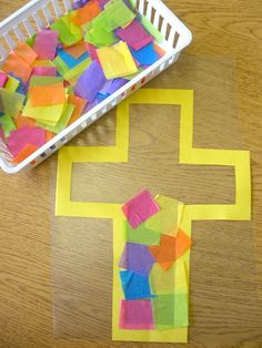 a cross made out of colored paper next to a basket with cut outs on it