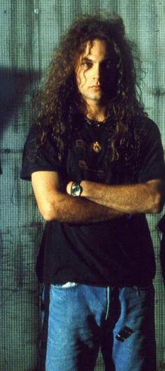 a man with long hair standing in front of a wall