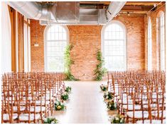 an indoor ceremony with rows of chairs and greenery