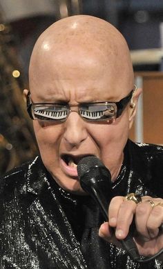 a bald man with glasses on singing into a microphone