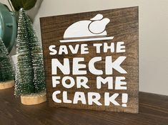 a wooden sign that says save the neck for me clark next to some christmas trees